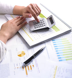 A photograph showing a hand surrounded by a calculator and numerous documents with charts and data. This photo represents the higher education strategic enrollment planning process where institutional leaders must use data to guide their future enrollment goals and processes.