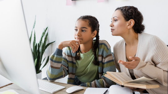 Daughter and parent seated at a computer to research colleges 