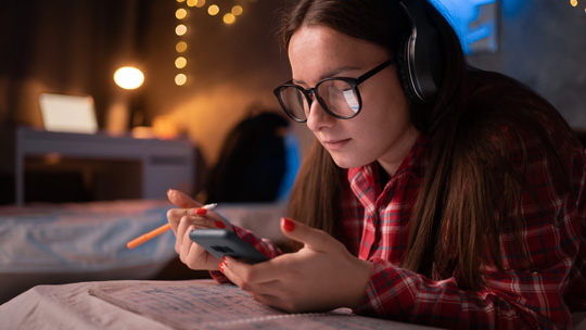 Blog: College Board Connections, female student looking at her phone while studying in her room