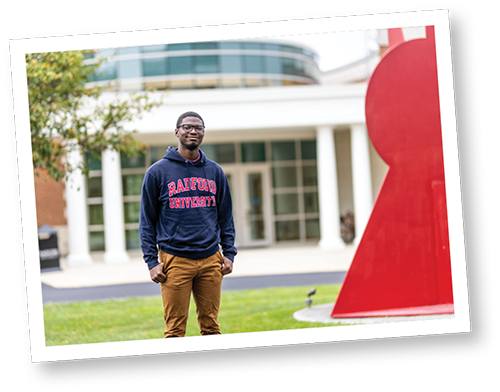 Male student wearing a Radford University sweatshirt in front of a university building