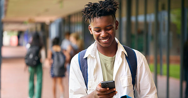 2025 E-Expectations Trend Report: Male high school student on his phone outside of classroom.
