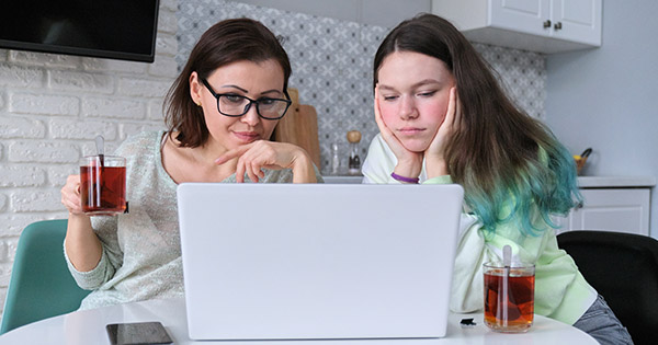 Mother and teenage daughter in kitchen looking at a laptop PC